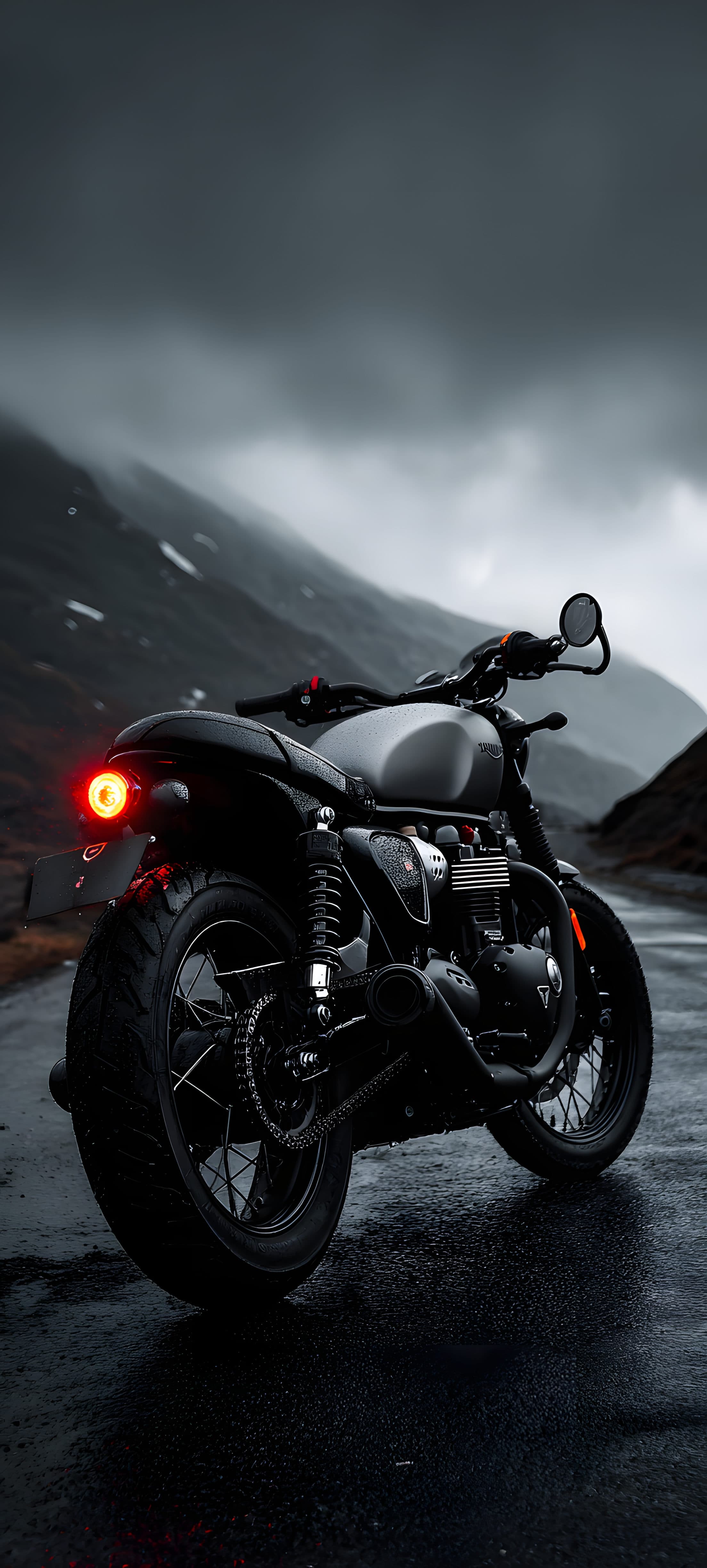 A black motorcycle parked on a wet road in a mountainous area under a cloudy sky.